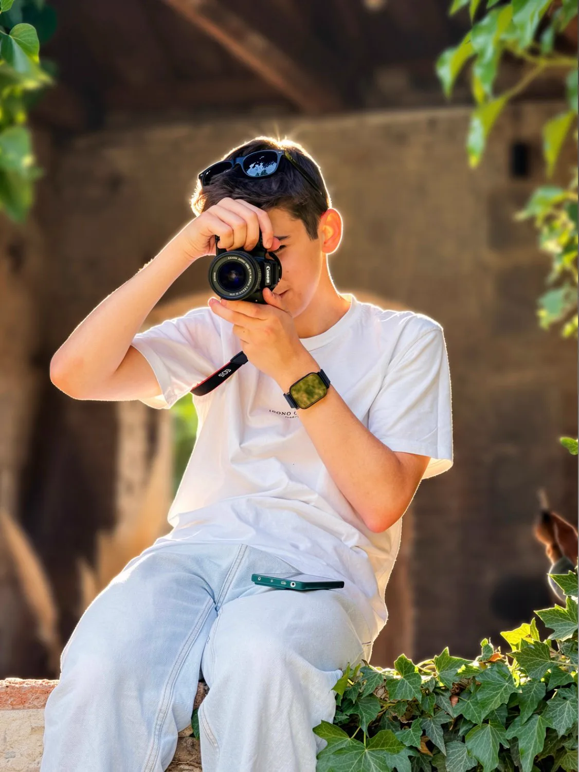 Sitting on a ledge holding a camera, surrounded by greenery