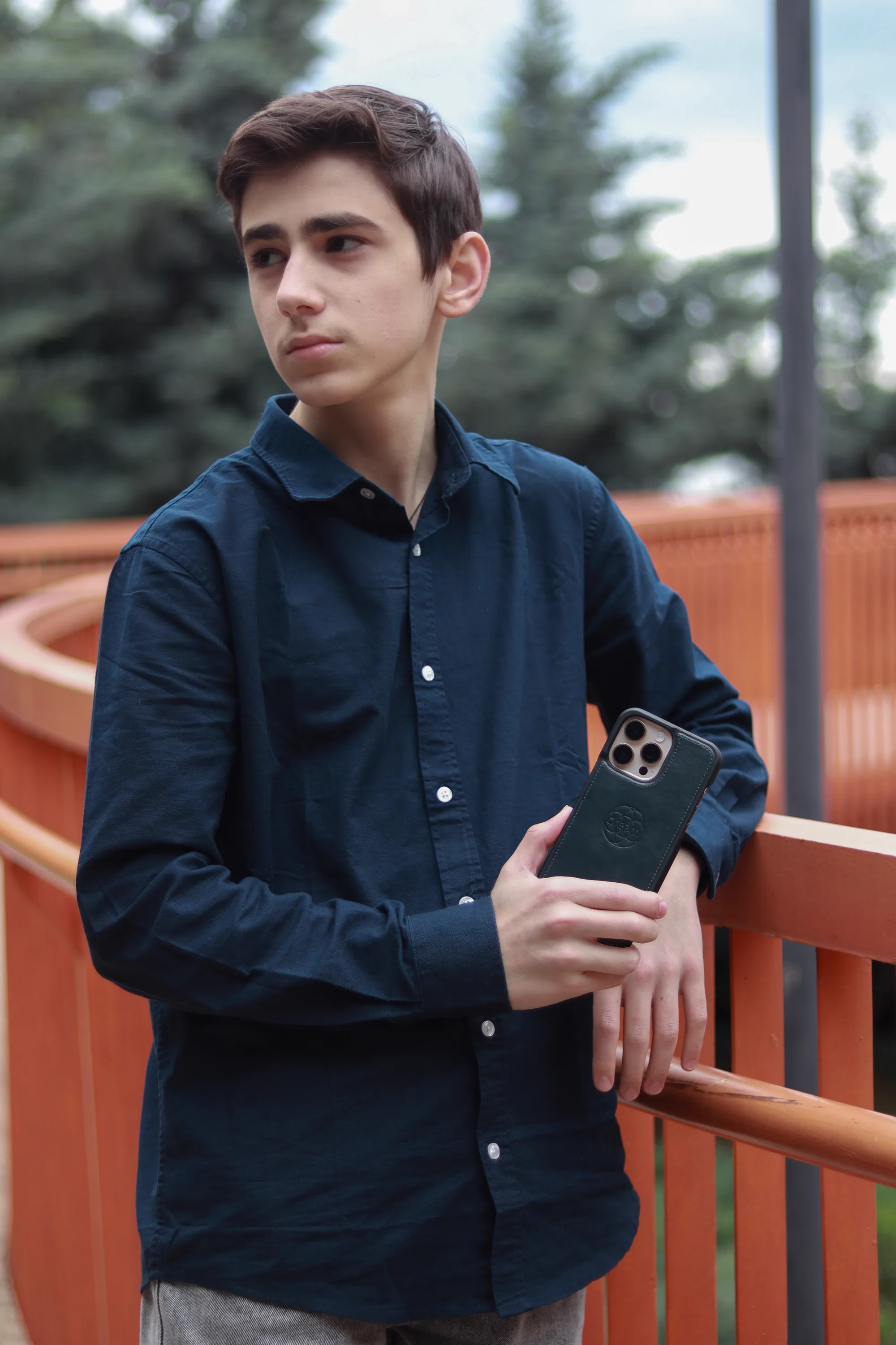 A young man in a navy shirt leaning on a railing, holding a smartphone