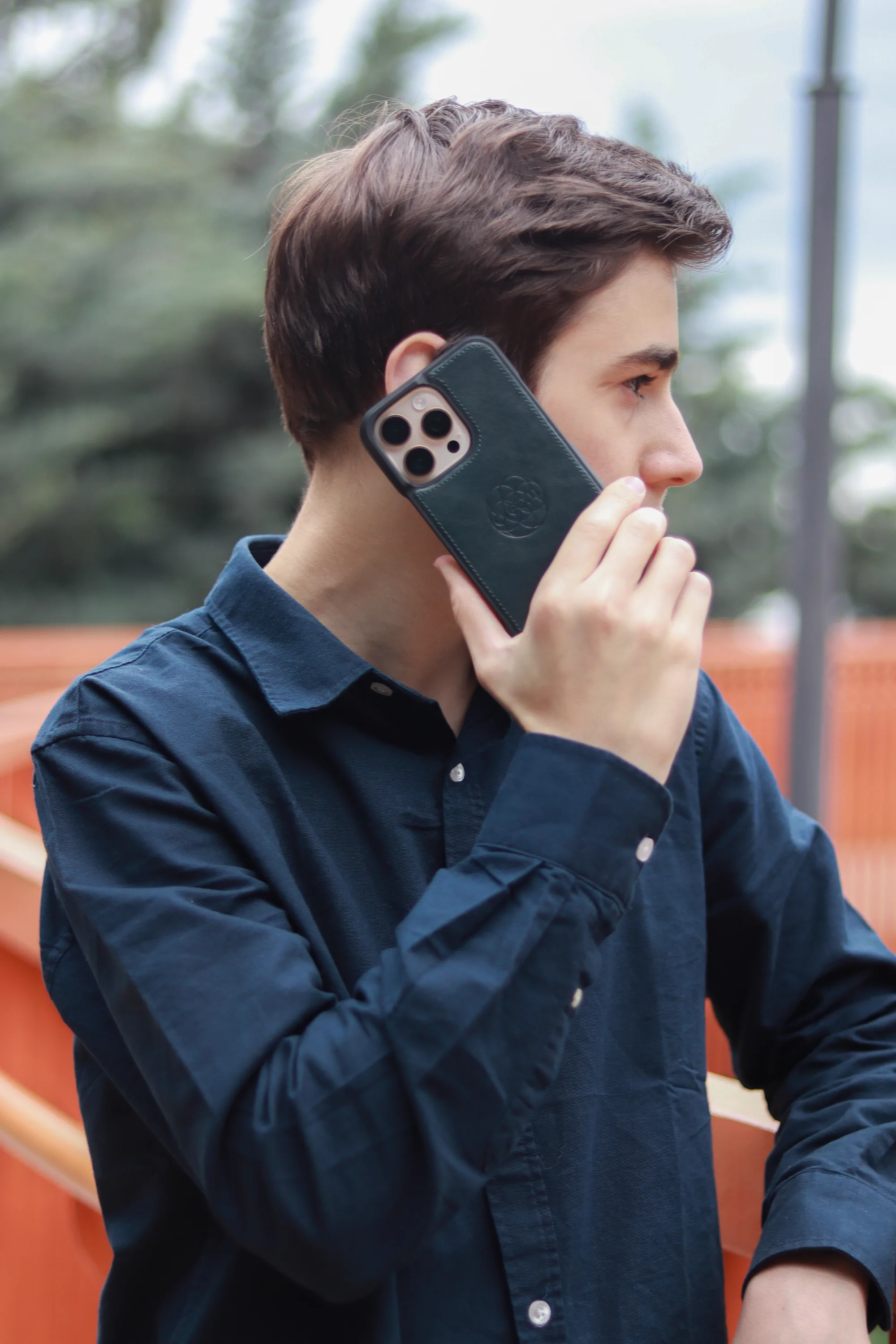 A young man in a navy shirt holding a smartphone to his ear outdoors