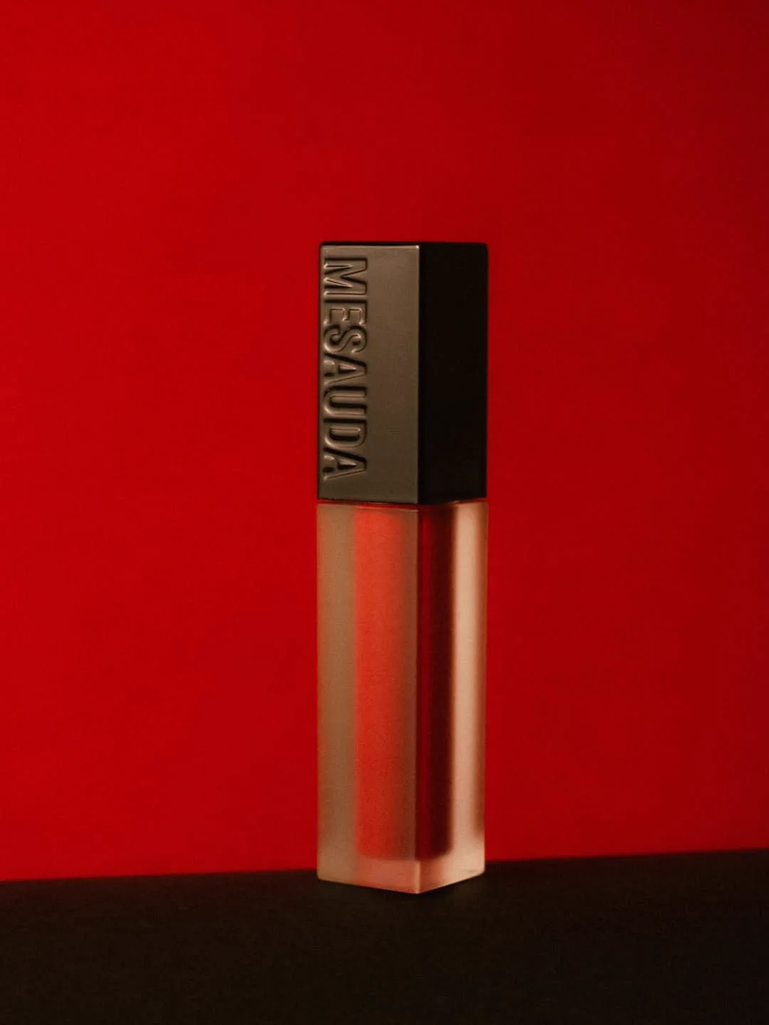 A lip gloss tube standing against a red background