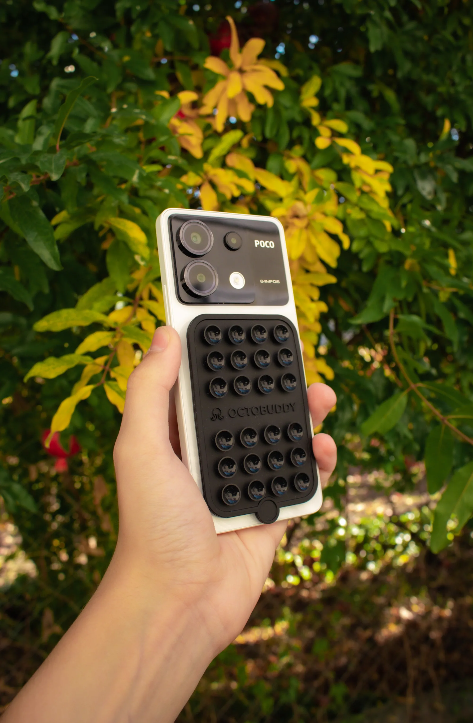 A hand holding a smartphone with a textured case against green foliage